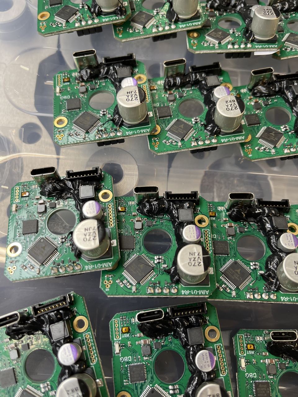 Close-up of AIM-01-R4 PCBAs showing USB-C, electrolytic capacitors, conformal coating, and QFP microcontrollers