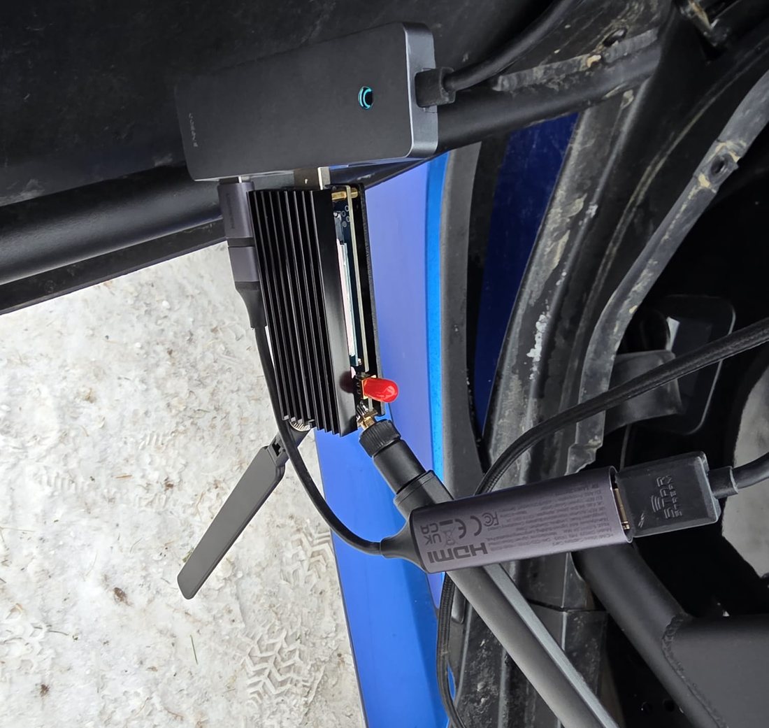 LTE modem on an M.2 adapter with a finned heatsink and SMA antenna, mounted on a roll cage bar next to a USB HDMI capture dongle