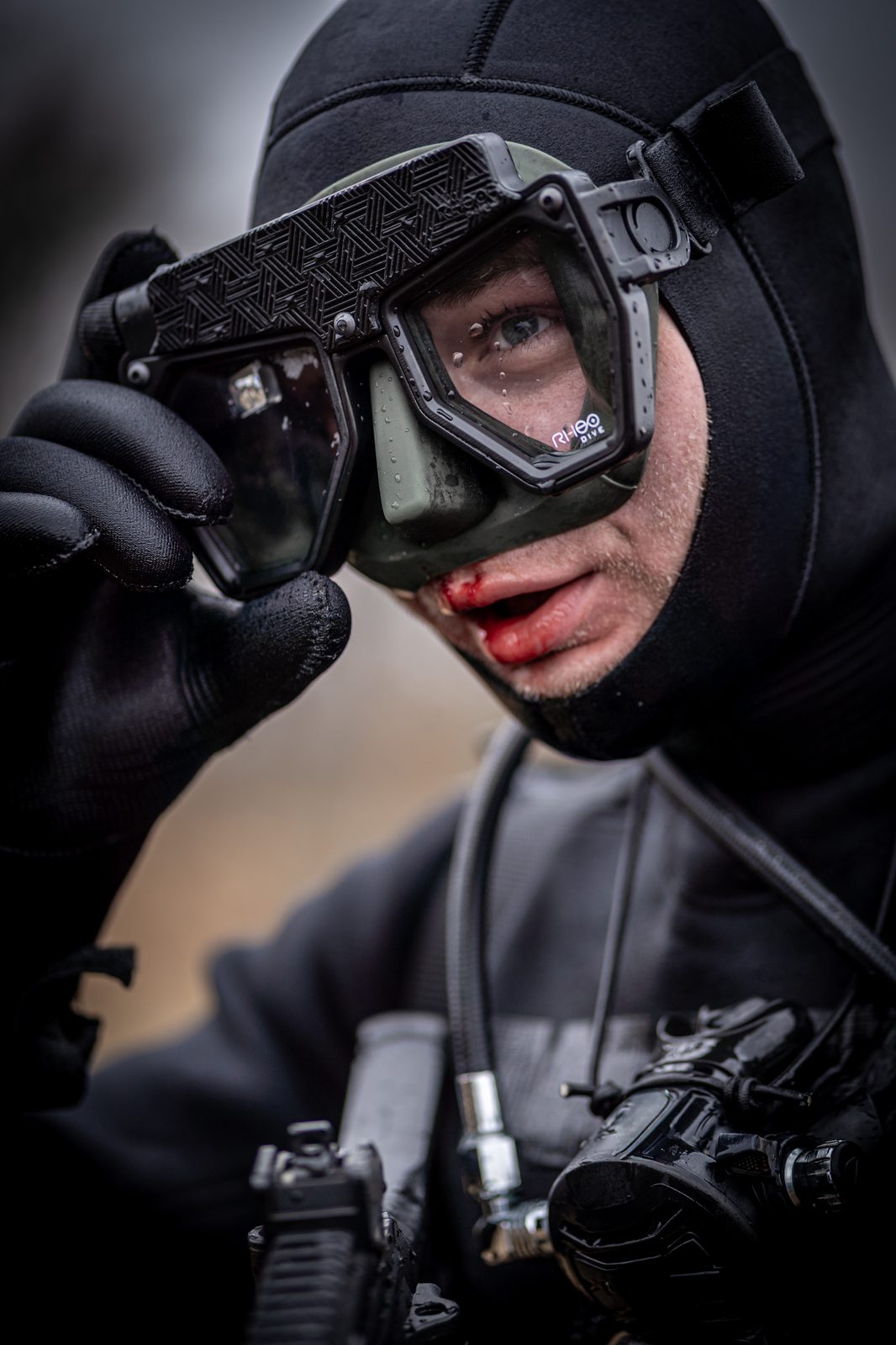 Close-up of diver adjusting Rheo Dive mask — RHEO DIVE logo visible on frame, HUD lens visible